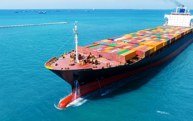 A large container ship navigates through the vast ocean, showcasing its impressive size against the blue waters.