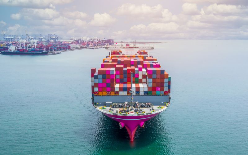 A large cargo ship sails through the ocean, filled with containers, representing the essence of direct export sales.